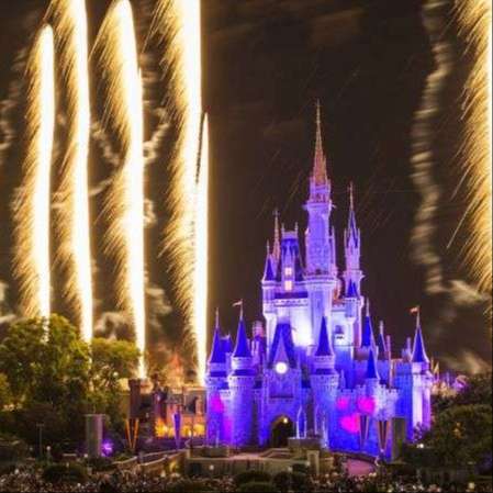 disney castle lit up purple at night with white fireworks columns