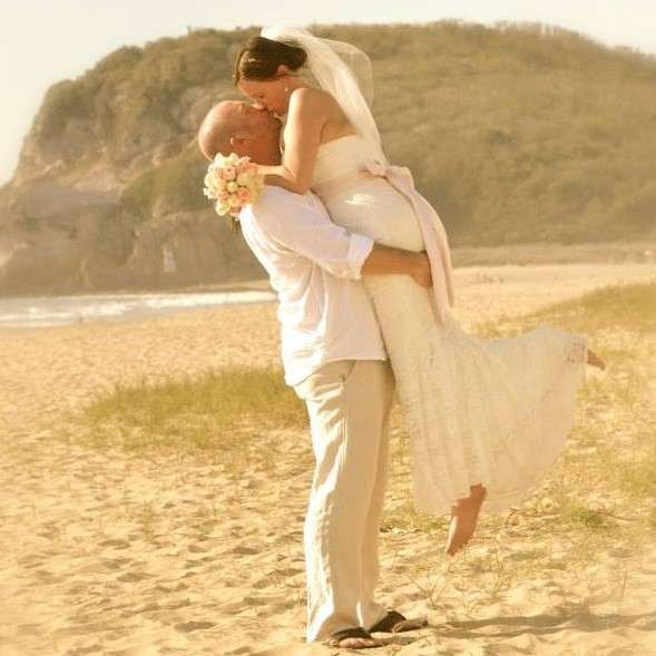 bride and groom on sandy beach in front of a rocky scrubby cliff