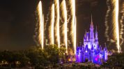 disney castle lit up purple at night with white fireworks columns
