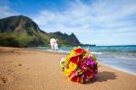bride's bouquet flowers in red, purple, yellow on a beach with hawaii green cliffs
