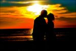 kissing couple silhouetted on beach at sunset